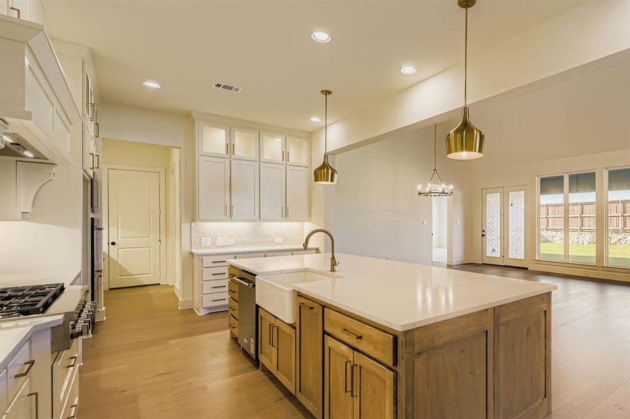 Kitchen with backsplash, decorative light fixtures, white cabinetry, light wood-type flooring, and recessed lighting