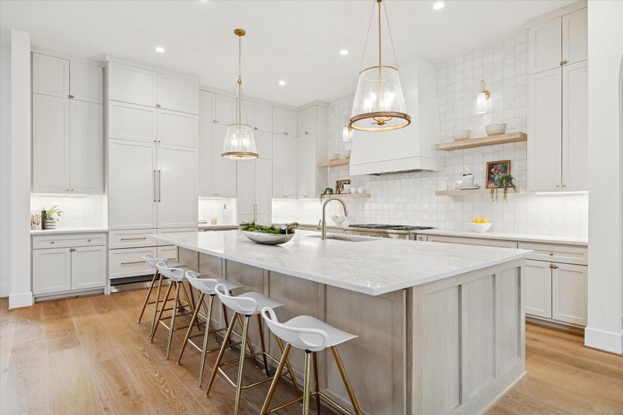 Bright gourmet kitchen with custom cabinetry, large island, built-in appliances, and sleek pendant lighting.
