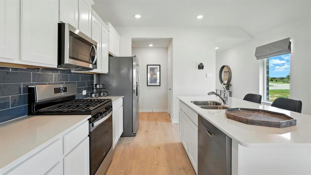 Kitchen featuring appliances with stainless steel finishes, white cabinets, backsplash, an island with sink, and recessed lighting