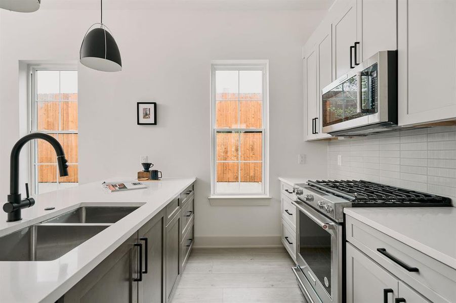 Modern kitchen featuring dual-tone cabinetry, stainless steel range and microwave, white quartz countertops, a double basin sink with matte black faucet, and light wood-finish flooring