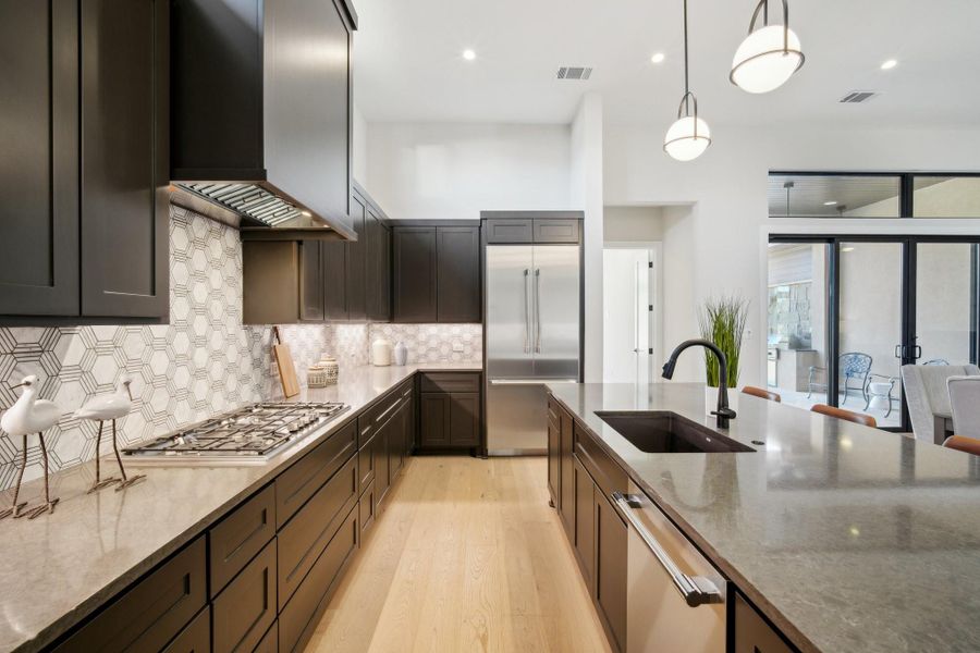 Kitchen featuring sink, wall chimney range hood, appliances with stainless steel finishes, and dark stone counters
