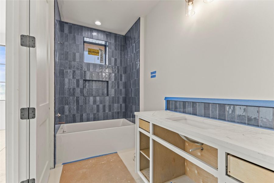 Bathroom featuring a built-in tub with dark rectangular wall tiling, an integrated shower niche, and a window