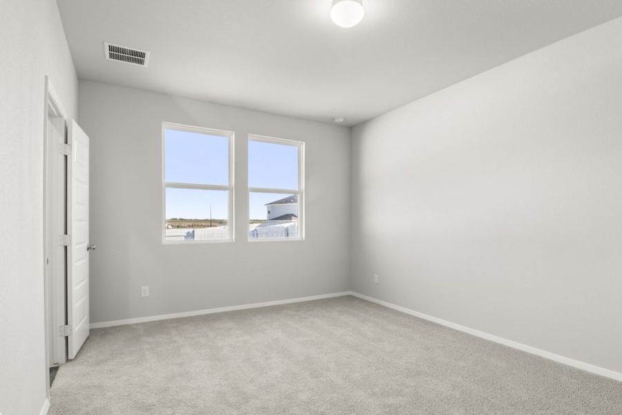 Image of a primary bedroom with tan carpeting and light grey painted walls with two windows Image of a primary bedroom with tan carpeting and light grey painted walls with two windows