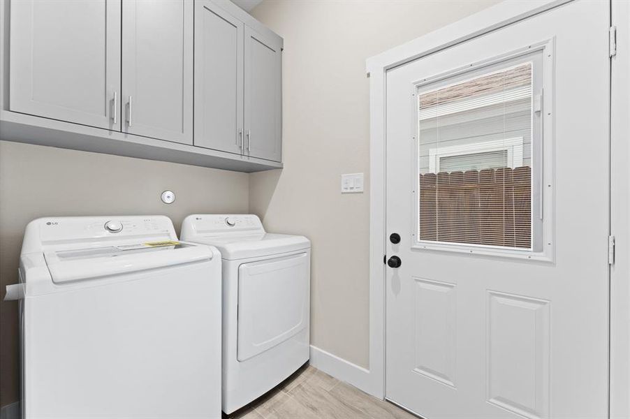 This laundry room features modern appliances, ample cabinetry, and a door with a window, offering natural light and backyard access.