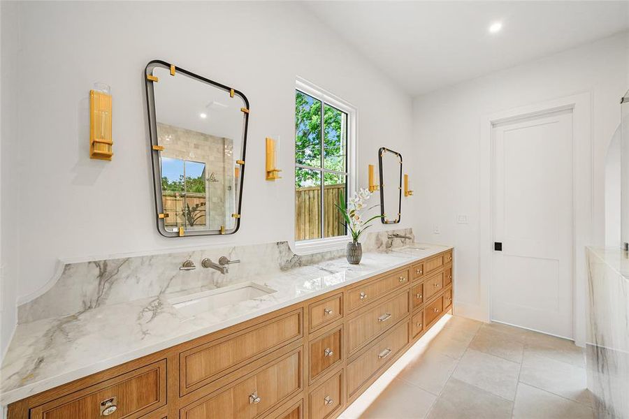 Double vanity featuring a light wood-finish cabinet with integrated lighting, a stone countertop with two undermount sinks, and wall-mounted faucets