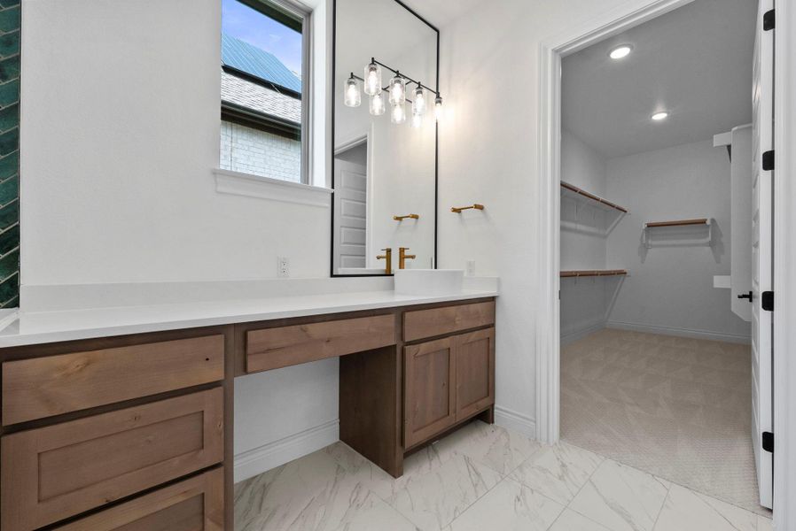 Primary suite vanity area with seating space, direct access to the expansive walk-in closet, and elegant gold fixtures.
