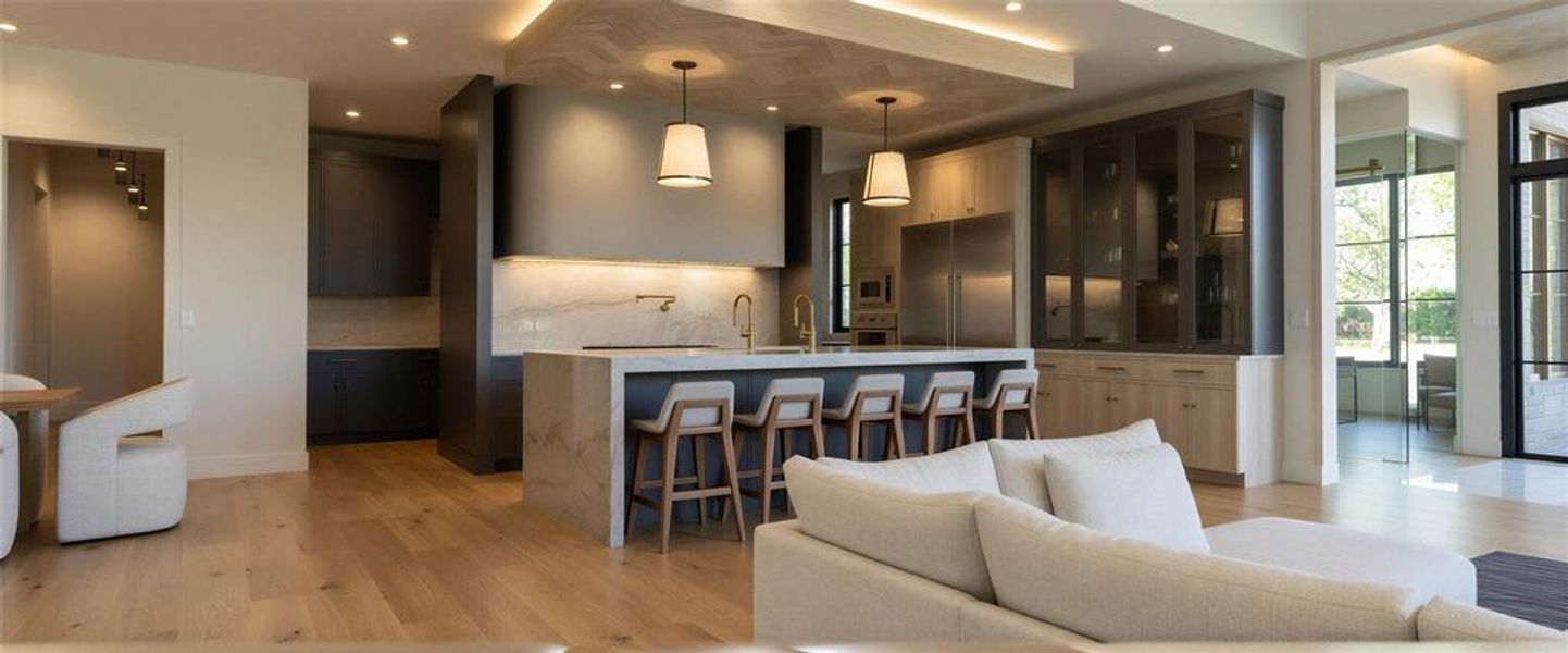 Living area with a high ceiling, light wood-style flooring, a glass covered fireplace, and built in features