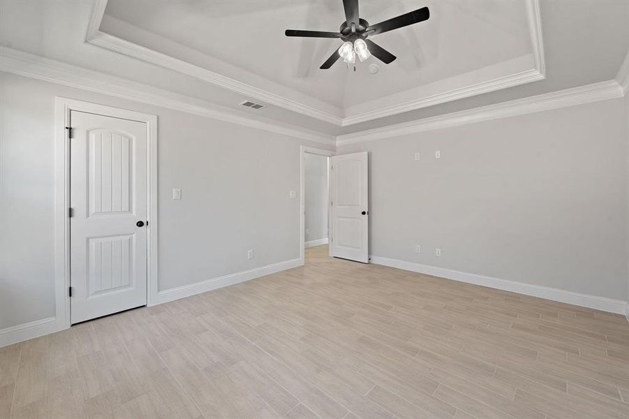 Unfurnished bedroom featuring light wood finished floors, ceiling fan, ornamental molding, and a tray ceiling
