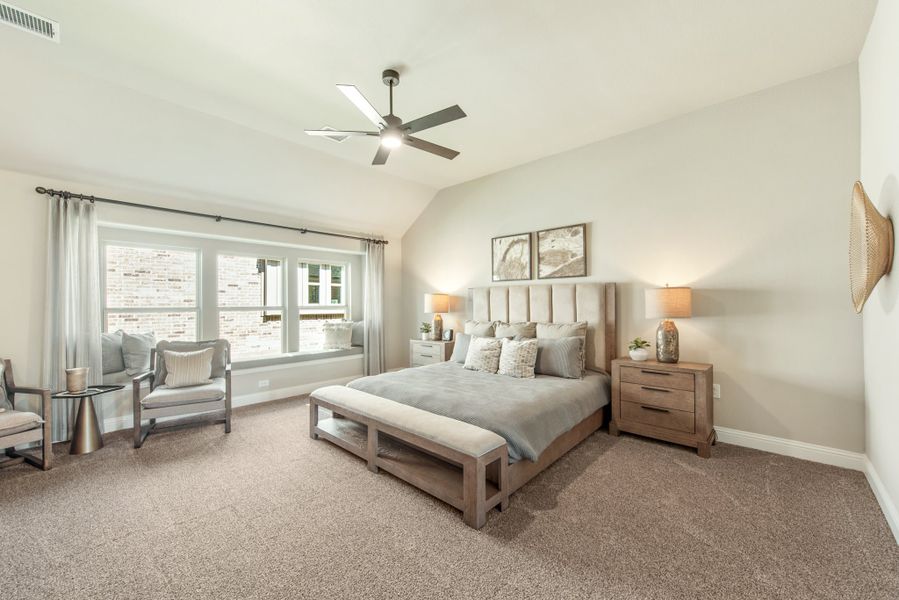 Spacious master bedroom with vaulted ceiling, ceiling fan, carpet floors, and large window seat area