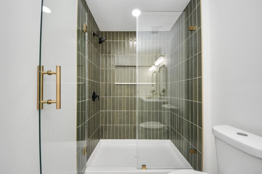 A striking walk-in shower framed by sleek glass and accented with bold brass hardware. Vertical olive-toned tile adds depth and sophistication, while matte black fixtures bring a modern edge. Clean lines and thoughtful details make this shower both functional and visually stunning.