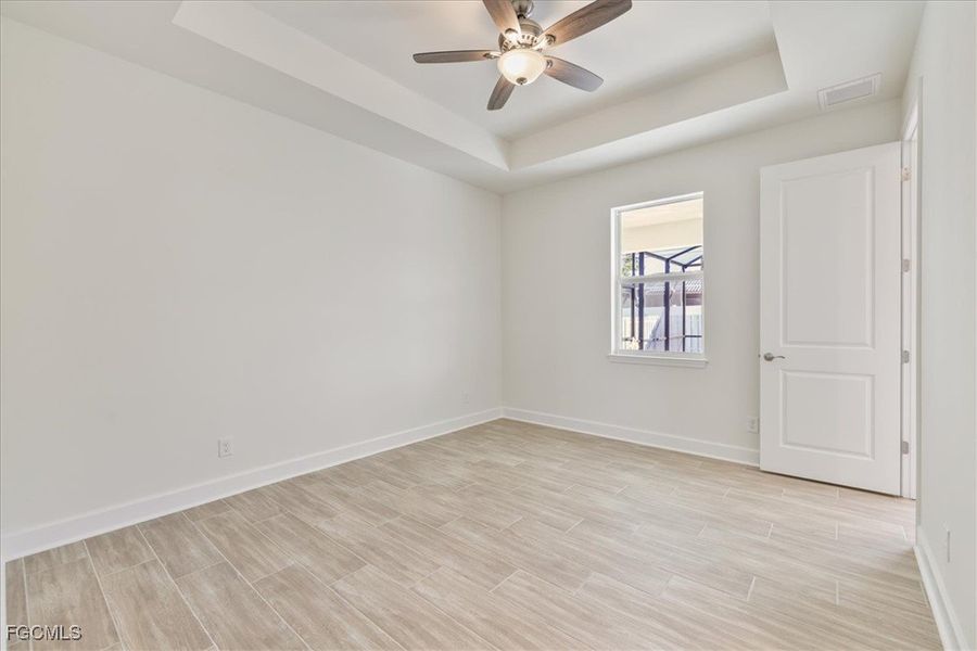 Empty room with a raised ceiling, wood finish floors, and ceiling fan