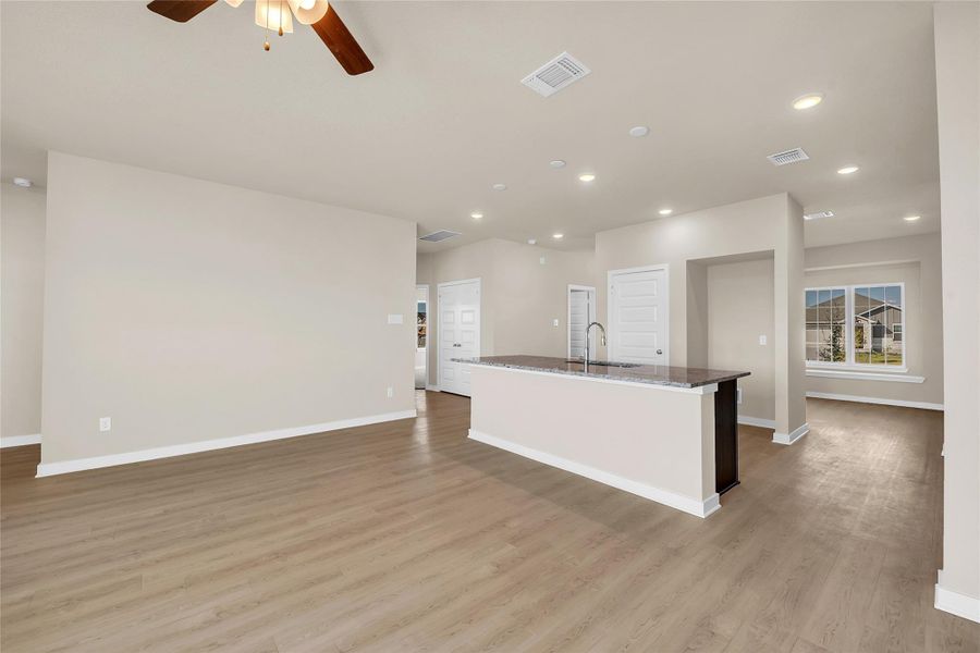 Kitchen with an island with sink, recessed lighting, ceiling fan, dark stone counters, and light wood finished floors