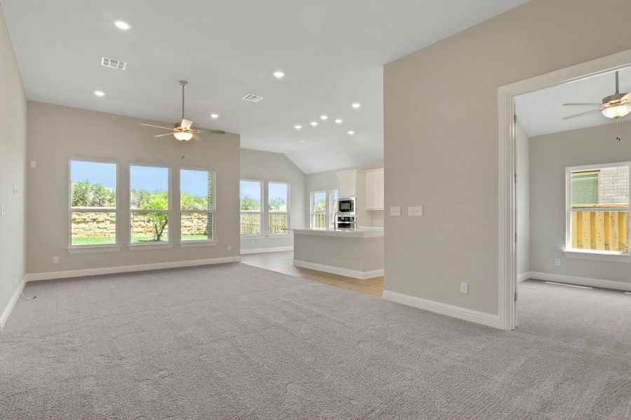 Unfurnished living room with visible vents, light colored carpet, baseboards, and ceiling fan