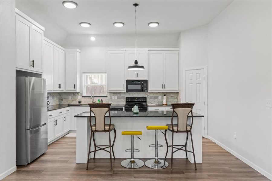 Kitchen featuring black appliances, a kitchen island, white cabinets, and a kitchen bar