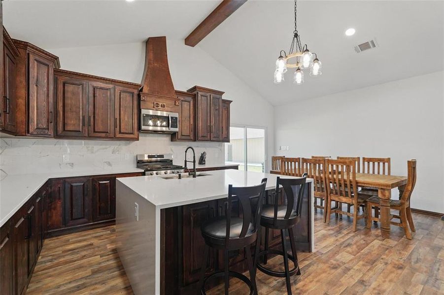 Kitchen with dark brown cabinets, a kitchen bar, decorative backsplash, appliances with stainless steel finishes, and high vaulted ceiling Kitchen with dark brown cabinets, a kitchen bar, decorative backsplash, appliances with stainless steel finishes, and high vaulted ceiling