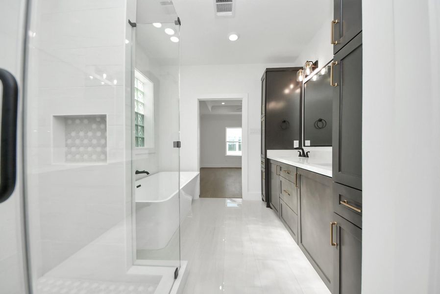 A modern bathroom showcasing dark cabinetry, sleek fixtures, a glass-enclosed shower, and a separate soaking tub. White walls and natural light from a large window create a bright, spa-like atmosphere.
