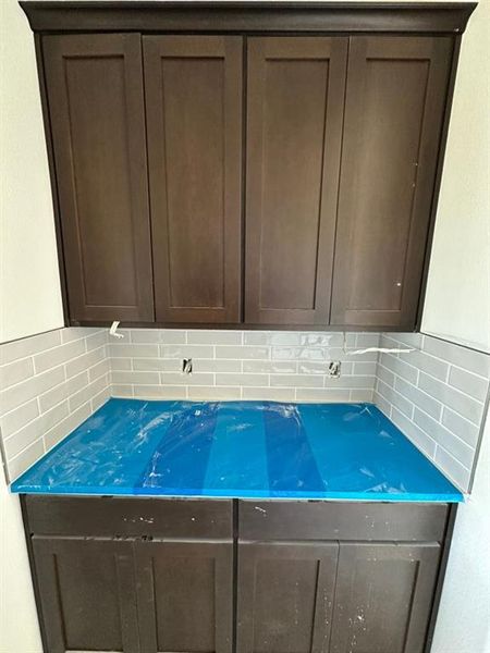 Custom cabinetry with dark wood-finish, light gray subway tile backsplash, and a protective-wrapped countertop