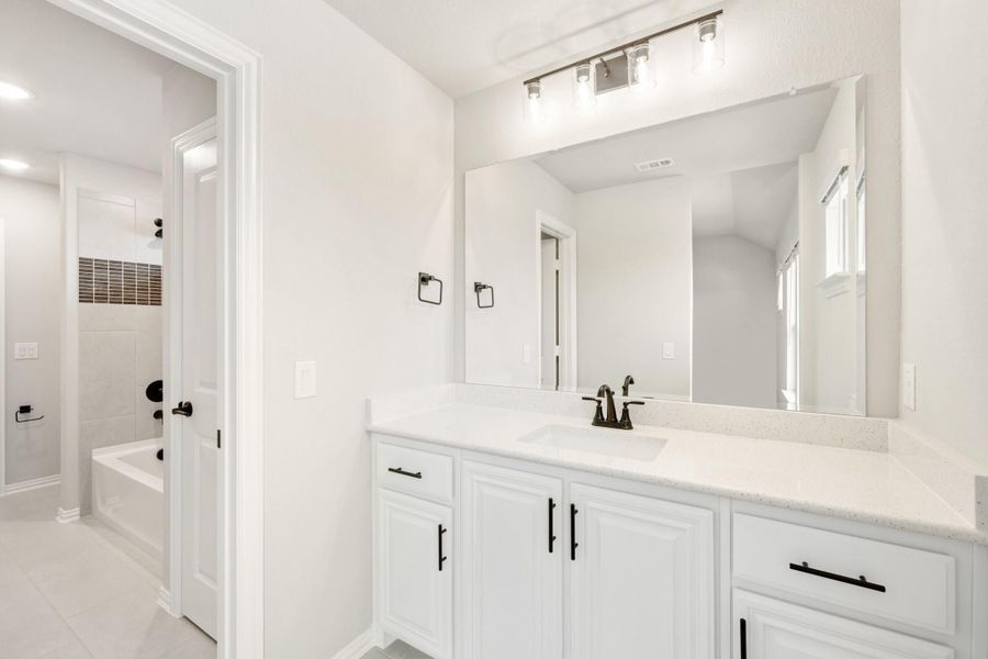 Bathroom with white vanity, quartz countertop, large mirror, and separate soaking tub room with tiled shower.