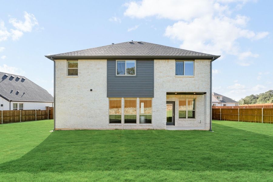 Rear view of two-story brick home with gray siding accent, large windows, covered patio, and fenced backyard