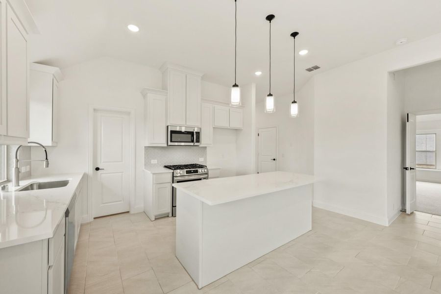 White kitchen with center island, pendant lights, stainless steel appliances, and white quartz countertops