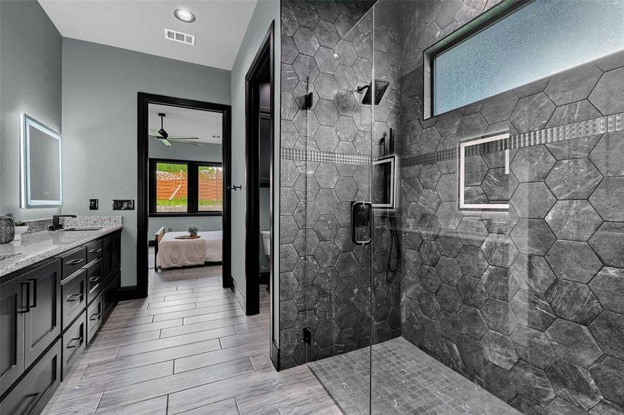 Bathroom featuring ensuite bathroom, double vanity, a stall shower, wood finished floors, and ceiling fan Bathroom featuring ensuite bathroom, double vanity, a stall shower, wood finished floors, and ceiling fan