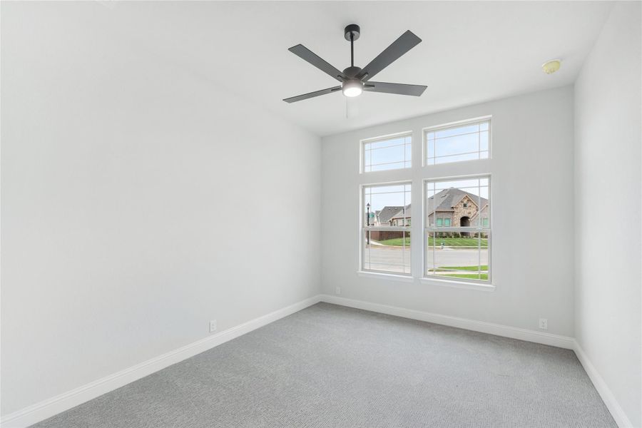 Empty bedroom with gray carpet, ceiling fan, and large windows overlooking a neighborhood street Empty bedroom with gray carpet, ceiling fan, and large windows overlooking a neighborhood street