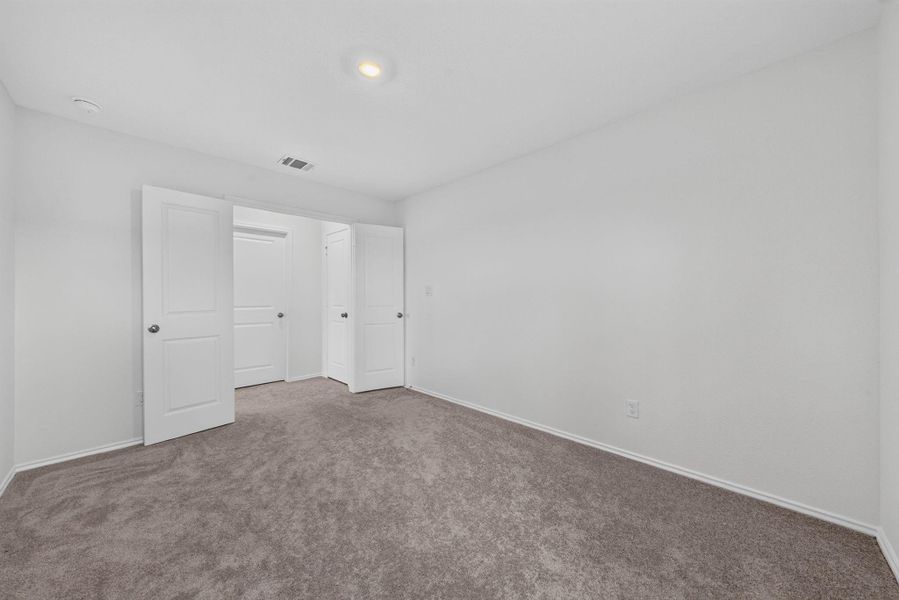 A spacious and inviting bedroom features plush carpeting and multiple closet doors, ready for personalized touches. A spacious and inviting bedroom features plush carpeting and multiple closet doors, ready for personalized touches.