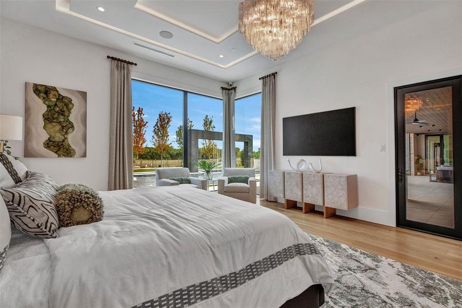 Bedroom with access to outside, a chandelier, light wood finished floors, and a tray ceiling Bedroom with access to outside, a chandelier, light wood finished floors, and a tray ceiling