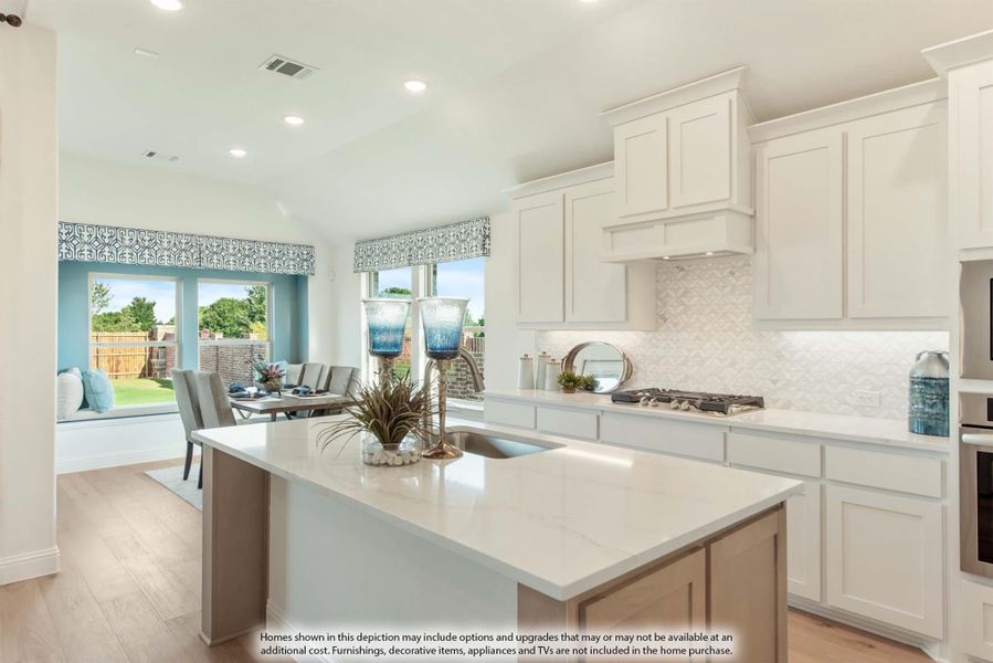 Kitchen with white cabinets, large center island, quartz countertops, and tile backsplash open to dining area with windows.