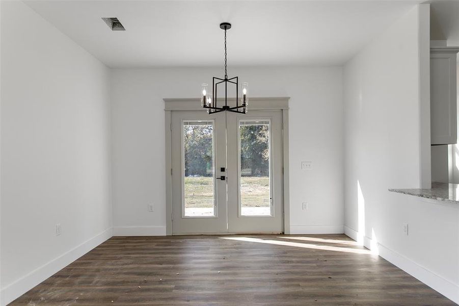 Unfurnished dining area with french doors, an inviting chandelier, and dark wood-type flooring