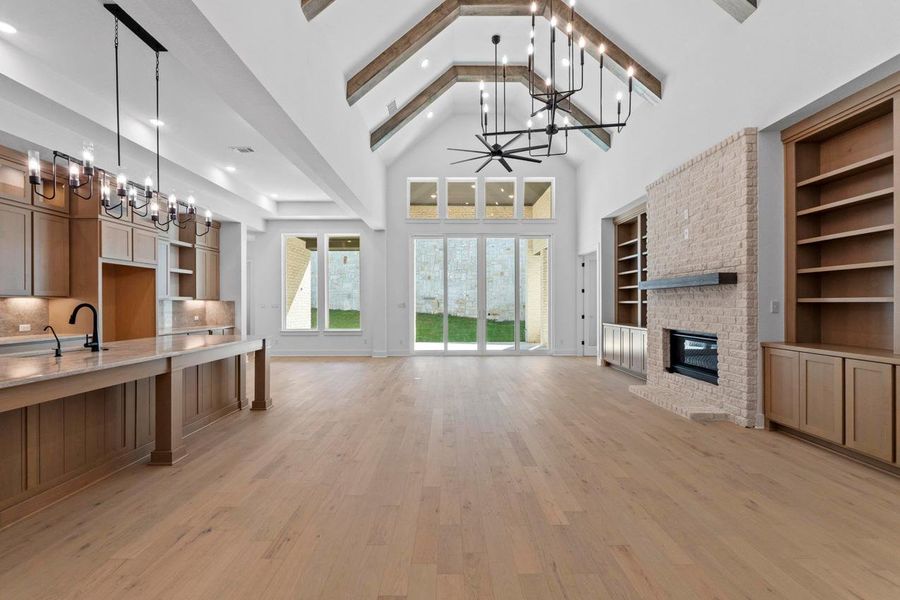 Unfurnished living room with a chandelier, light wood-style flooring, a fireplace, high vaulted ceiling, and built in shelves Unfurnished living room with a chandelier, light wood-style flooring, a fireplace, high vaulted ceiling, and built in shelves