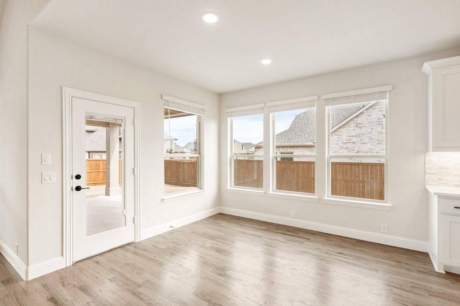 Bright empty room with light wood floors, large windows, and a glass-panel door leading to the backyard