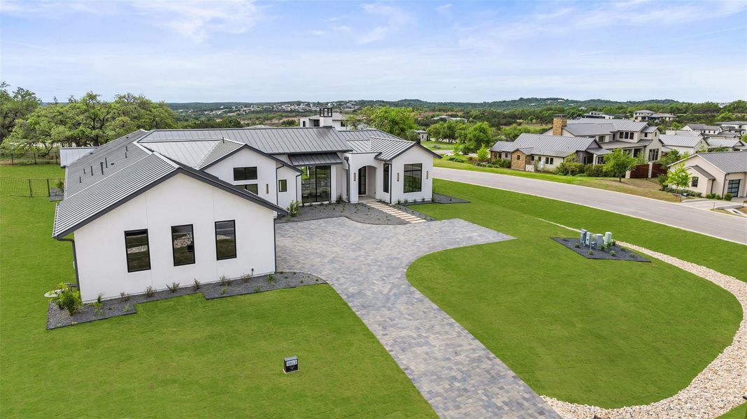 View of front facade featuring stucco siding, a standing seam roof, decorative driveway, a front yard, and metal roof View of front facade featuring stucco siding, a standing seam roof, decorative driveway, a front yard, and metal roof