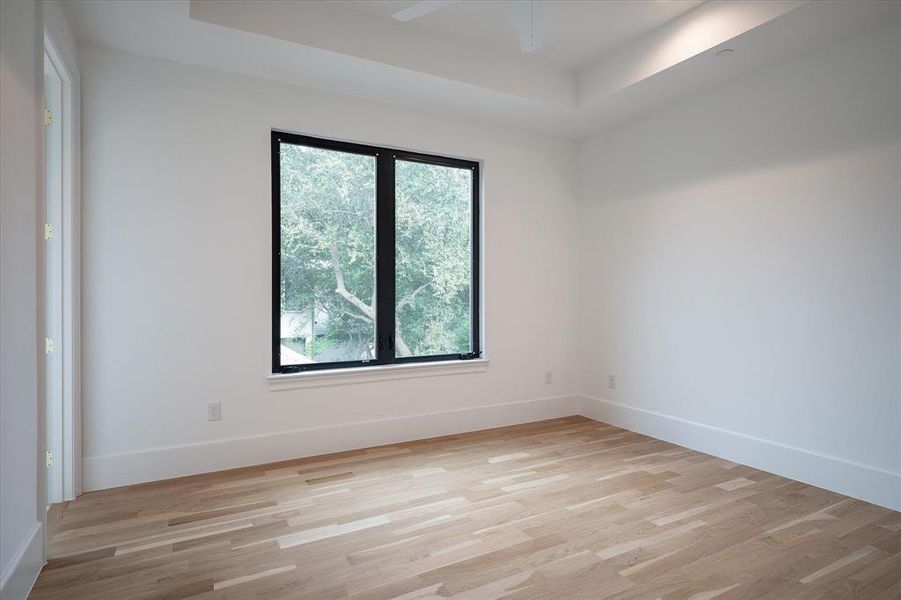 Spare room with a tray ceiling, ceiling fan, and light hardwood / wood-style floors