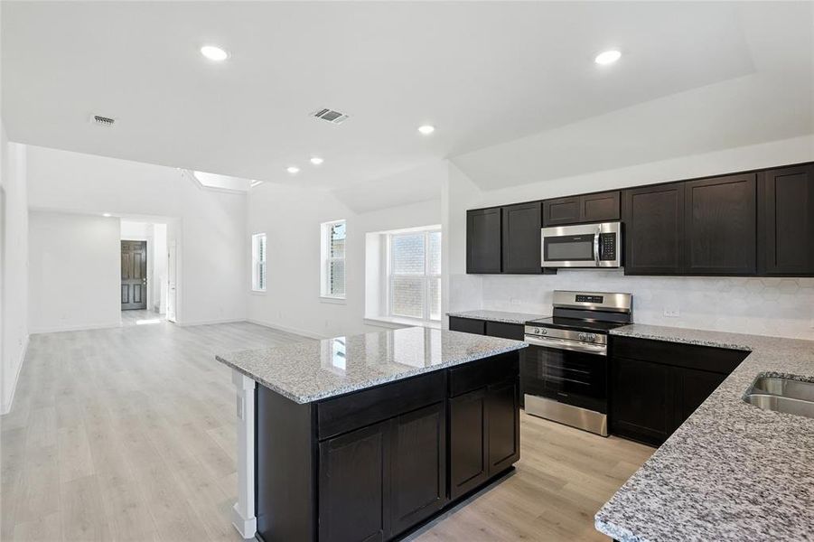 Kitchen with light stone counters, stainless steel appliances, light wood finished floors, open floor plan, and a kitchen island Kitchen with light stone counters, stainless steel appliances, light wood finished floors, open floor plan, and a kitchen island