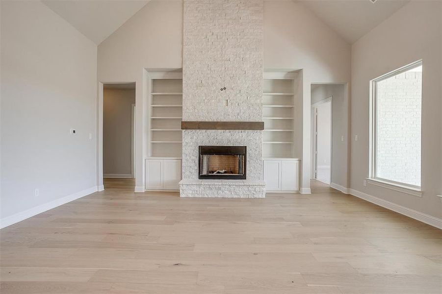 Unfurnished living room with high vaulted ceiling, a stone fireplace, built in shelves, and light hardwood / wood-style floors