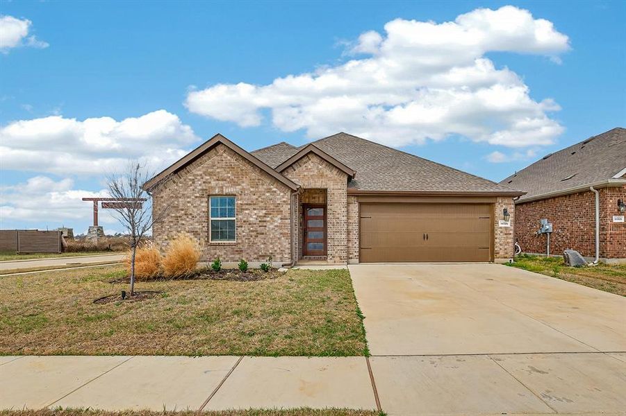 View of front of home featuring brick siding, driveway, roof with shingles, and an attached garage