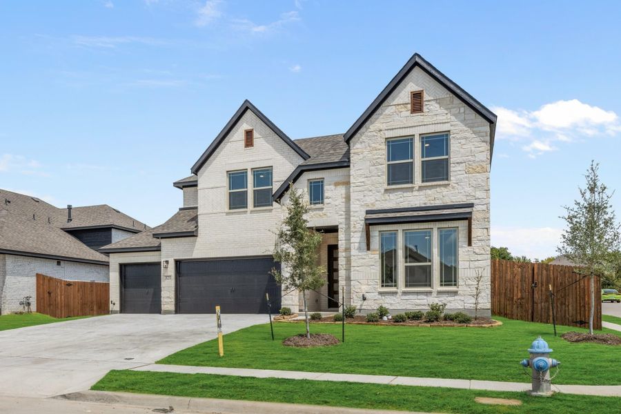 Two-story home with stone and brick exterior, two-car garage, and green front lawn