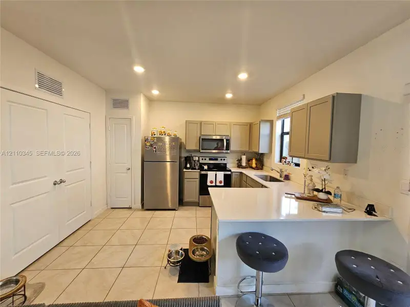 Kitchen featuring light-toned cabinetry, stainless steel appliances, a peninsula with stone-surface countertop, and ceramic tile flooring