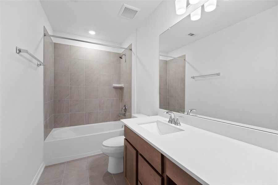 Secondary bath features tile flooring, bath/shower combo with tile surround, stained wood cabinets, beautiful light countertops, mirror, sleek fixtures and modern finishes.