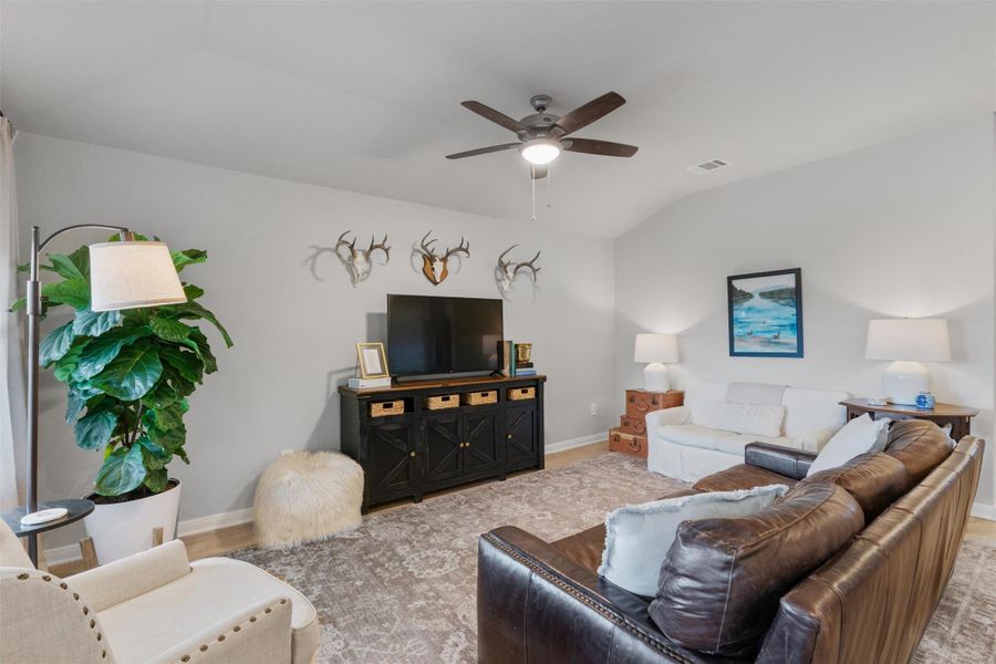 Spacious living area featuring vaulted ceilings, light gray wall tones, wood-finish flooring, and a ceiling fan with integrated lighting Spacious living area featuring vaulted ceilings, light gray wall tones, wood-finish flooring, and a ceiling fan with integrated lighting