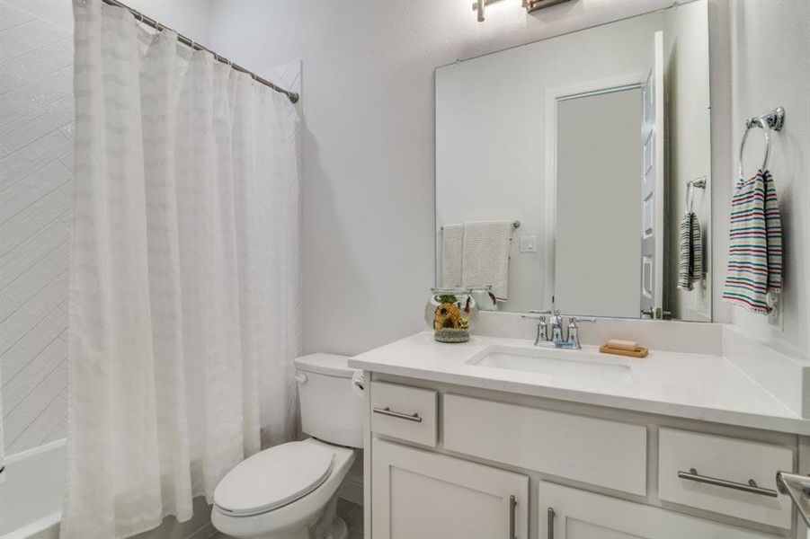 Full bathroom featuring toilet, vanity, and shower / bathtub combination with curtain Full bathroom featuring toilet, vanity, and shower / bathtub combination with curtain