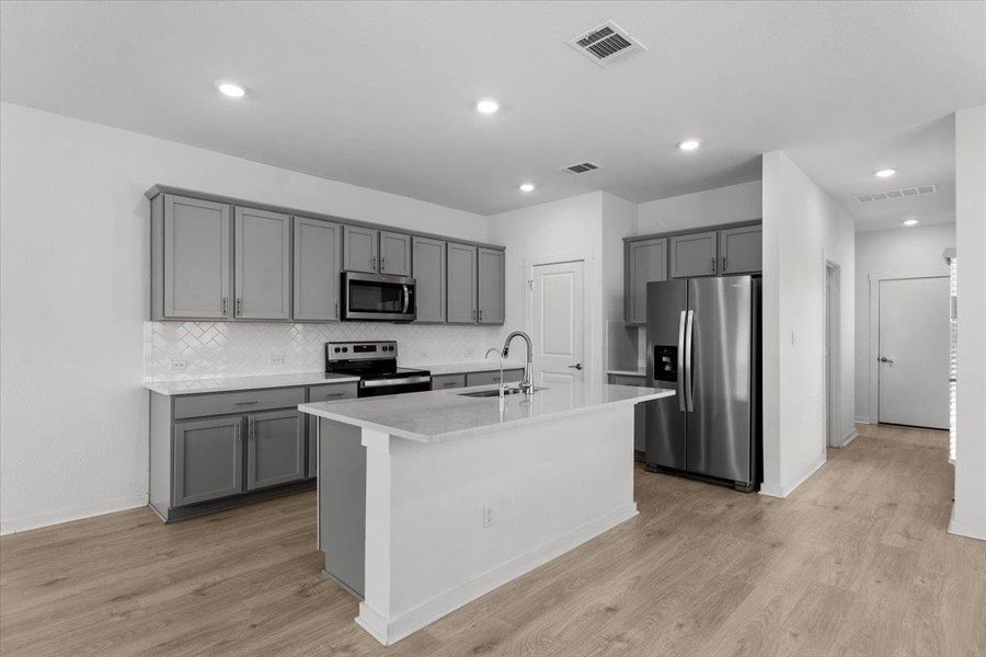 A well-appointed kitchen features stainless steel appliances, a center island with a sink, and sleek gray cabinetry.