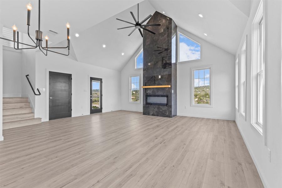 Unfurnished living room featuring a high ceiling, a fireplace, light wood finished floors, ceiling fan, and recessed lighting