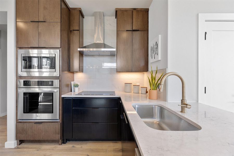 Kitchen featuring wall chimney range hood, appliances with stainless steel finishes, light stone countertops, and tasteful backsplash