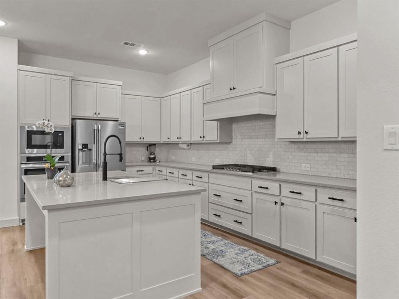 Kitchen with stainless steel appliances, a kitchen island with sink, and white cabinets