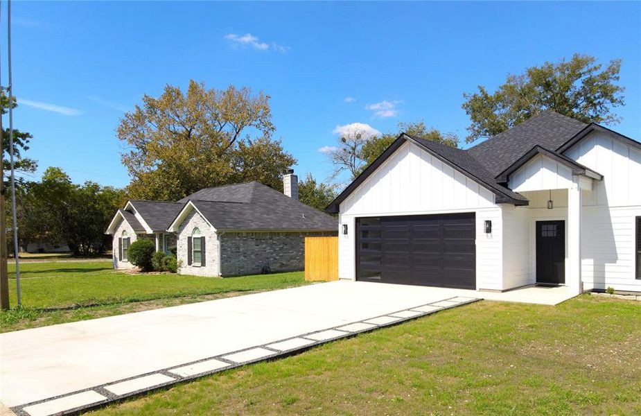 View of front of house with board and batten siding, a front lawn, concrete driveway, roof with shingles, and a garage View of front of house with board and batten siding, a front lawn, concrete driveway, roof with shingles, and a garage