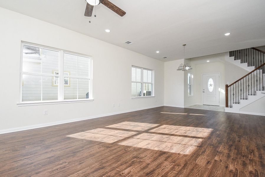 Spacious, empty room with hardwood floors, large windows, ceiling fan, and staircase leading upstairs. Bright, modern interior with a neutral color palette.