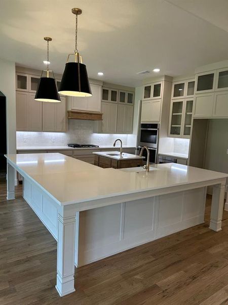 Kitchen featuring a kitchen bar, glass insert cabinets, recessed lighting, decorative backsplash, and dark wood-type flooring