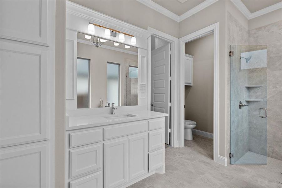 Bathroom featuring toilet, a shower with door, ornamental molding, and vanity.Not actual home. Previous built example.